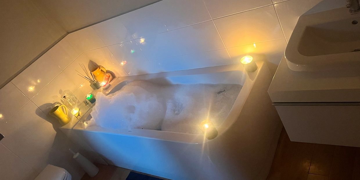 A cozy bathtub filled with bubbles, surrounded by lit candles and warm lighting.