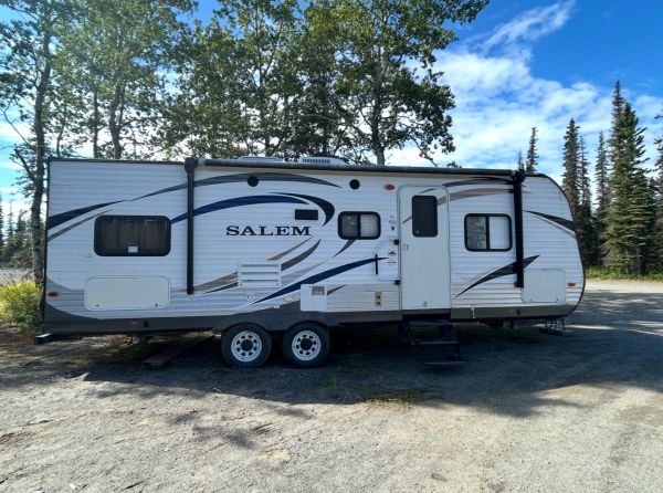 White Salem travel trailer parked on a dirt road with trees and blue sky.