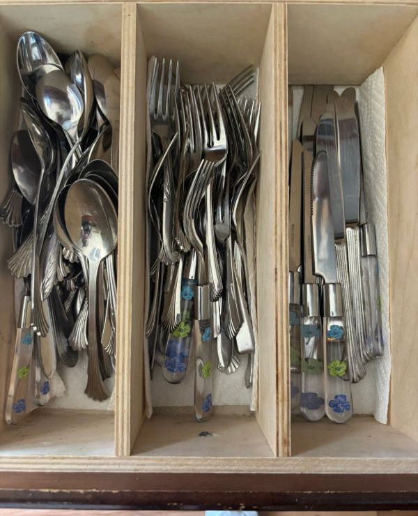 Organized cutlery set with spoons, forks, and knives in a wooden drawer.