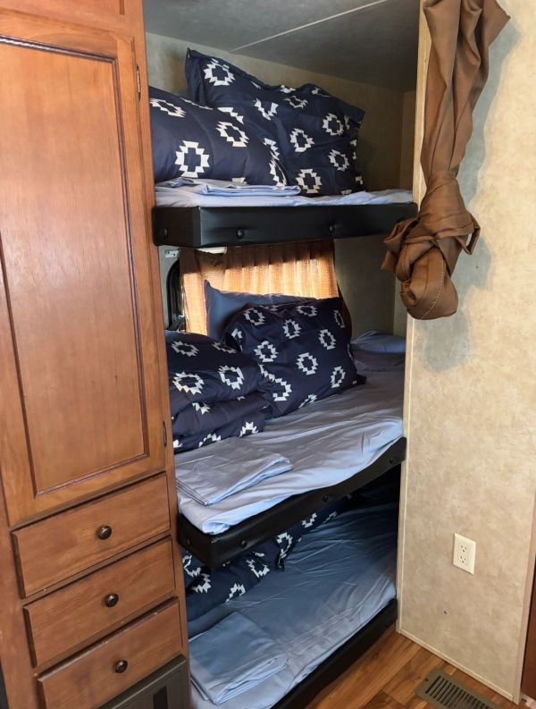 Triple bunk beds with blue patterned bedding in a compact room.