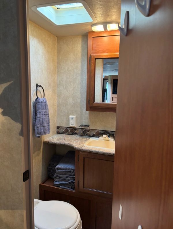 Compact bathroom with wooden cabinets, a small sink, and folded towels.