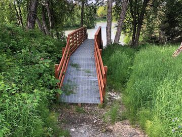 A small metal bridge in a lush green forest near a river.