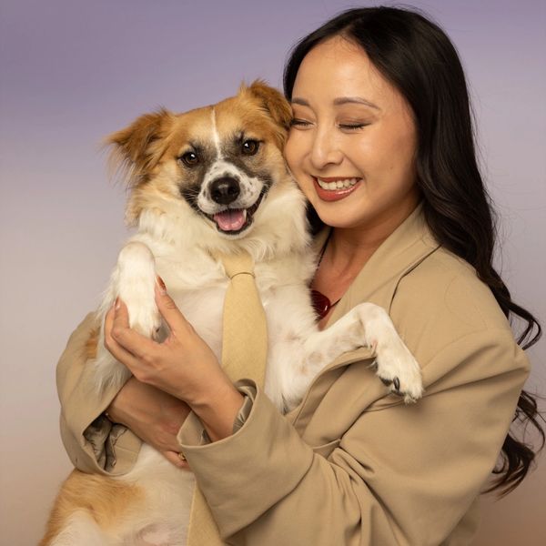 Woman in beige suit happily holding a dog wearing a matching beige tie.