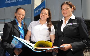 Three women in business attire reviewing documents outside a business center.