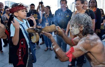 A traditional smoking ceremony performed by an elder with a child observing.