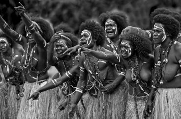 Group of indigenous women in traditional attire and face paint, energetically pointing and chanting.