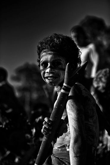 Black and white portrait of a child with face paint holding a spear.