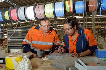 Two women in safety gear working with electrical wires in a workshop.