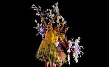 Three dancers in traditional attire performing with feathered props.