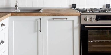 Modern kitchen with white cabinets, wooden countertop, and stainless steel appliances.