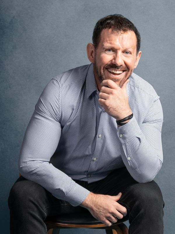 Modern headshot studio portrait of a middle aged professional man sitting on a black leather chair  