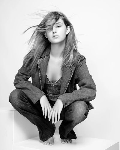 black and white portrait of  teenage model crouched low wearing jeans and a denim jacket with wind b