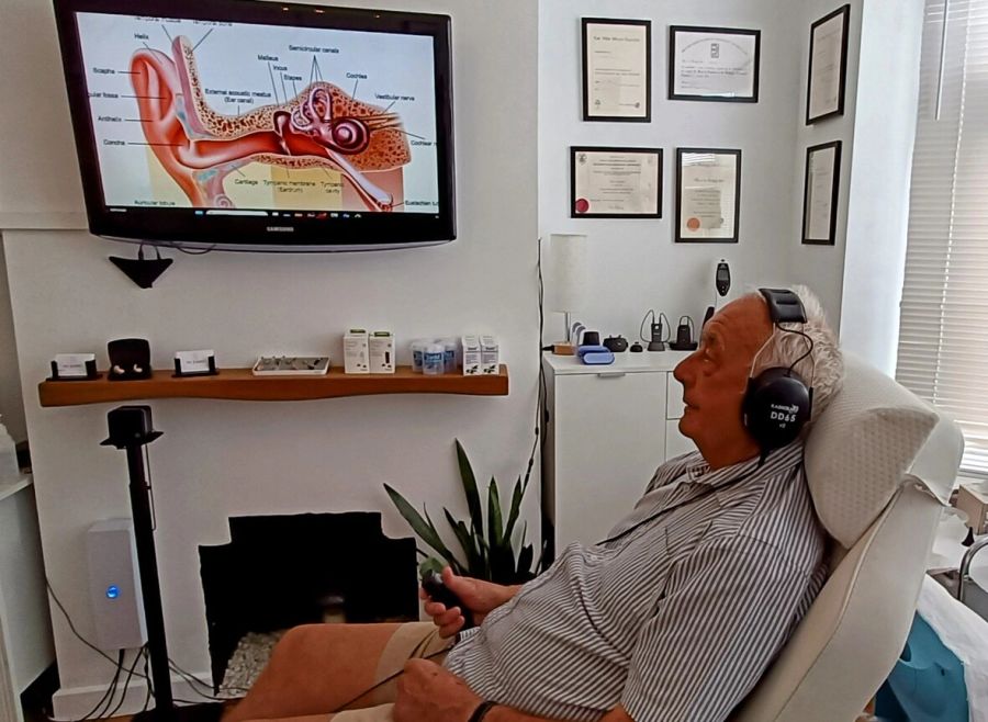 A patient in the consultation chair at mi Ears, with an ear diagram on screen as results are explained