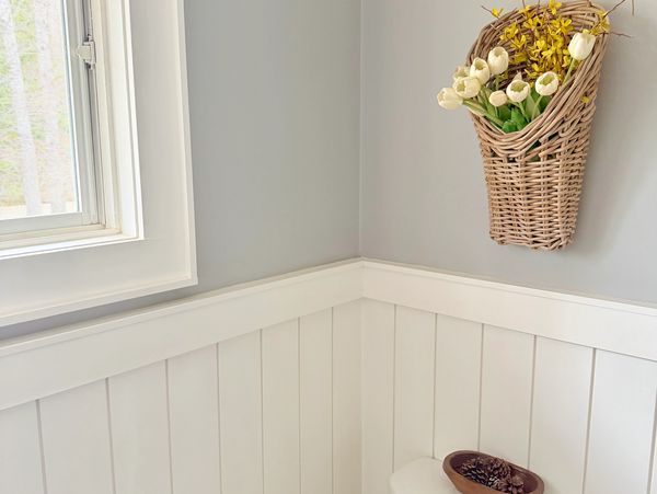 Bright corner of a room with a window and a wicker basket of flowers on the wall.