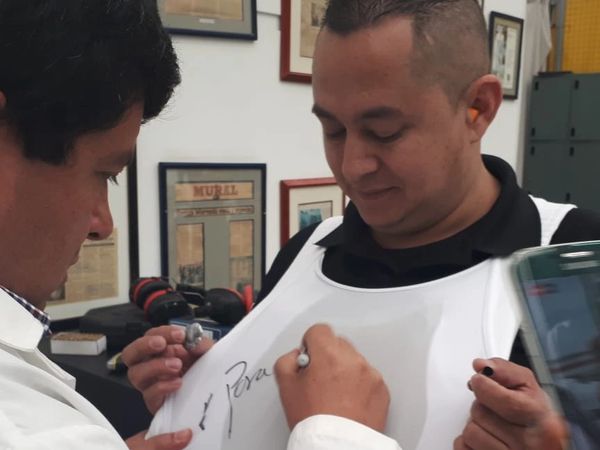 A man signing another man's white armor vest indoors.
