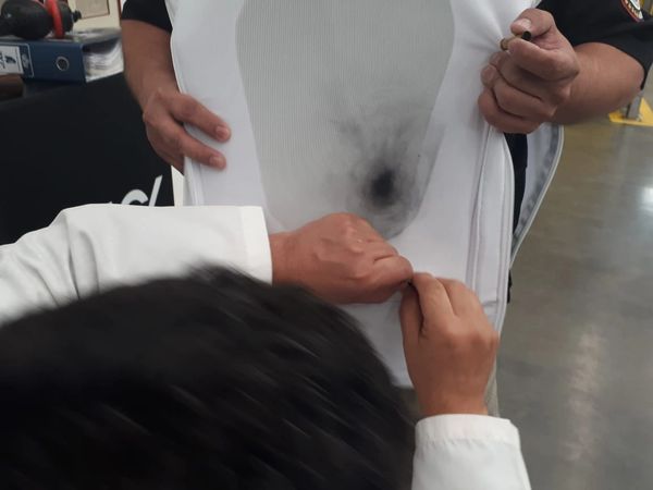 Person inspecting a bullet hole in a bulletproof vest.