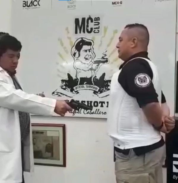 Man in white coat aiming a gun at another man with hands behind back indoors.