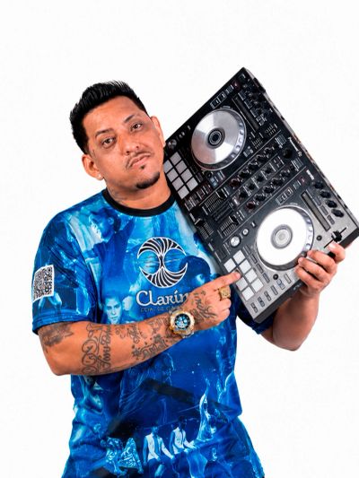 Man holding a DJ controller, wearing a blue graphic t-shirt with tattoos and a watch.