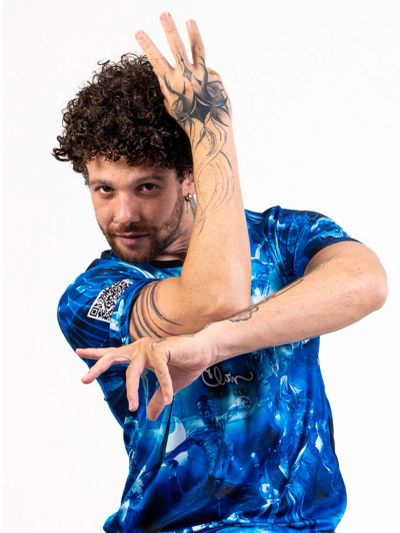 Man with curly hair striking a dynamic pose in a blue patterned shirt.