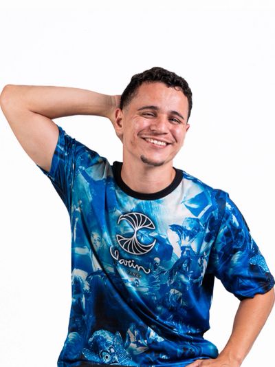 Smiling man with hand behind head wearing a blue patterned shirt.