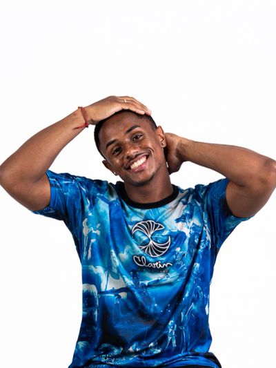 Smiling man in a vibrant blue shirt posing with hands on his head.