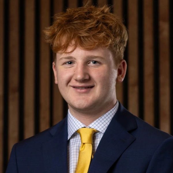 Young man in a suit with a yellow tie smiling at the camera.