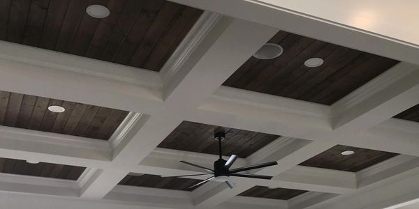 Modern ceiling design with wooden panels, recessed lights, and a large black ceiling fan.