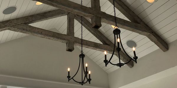 Rustic wooden beams and black chandeliers adorn a high white ceiling.