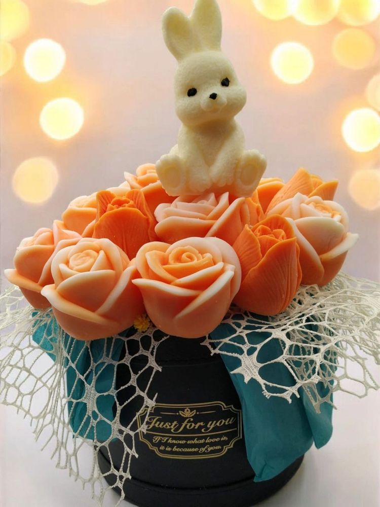A cute bunny sits atop peach-colored roses in a decorative black box with lace and teal fabric.