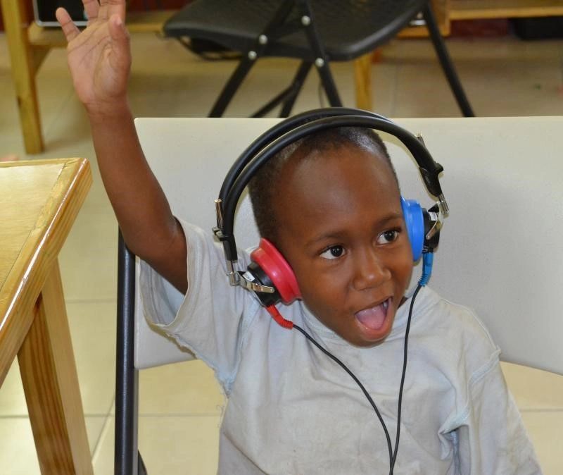 Excited child with headphones, raising hand and smiling.