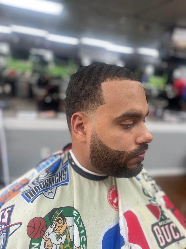 Man with a fresh fade haircut and a well-groomed beard in a barbershop.