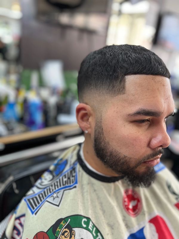Man with a fresh haircut and beard trim wearing a sports-themed barber cape.