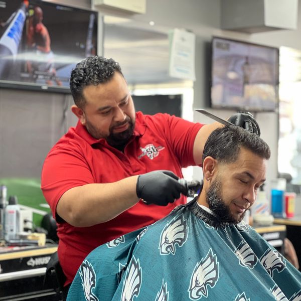 Barber giving a customer a haircut in a lively barbershop.