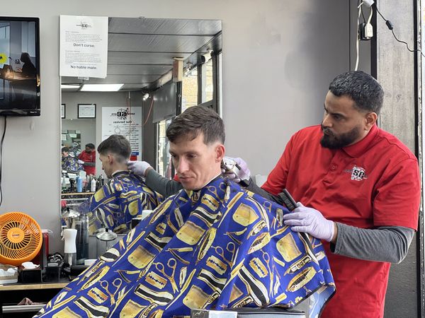 Barber giving a haircut to a man in a vibrant blue cape with barber tools pattern.
