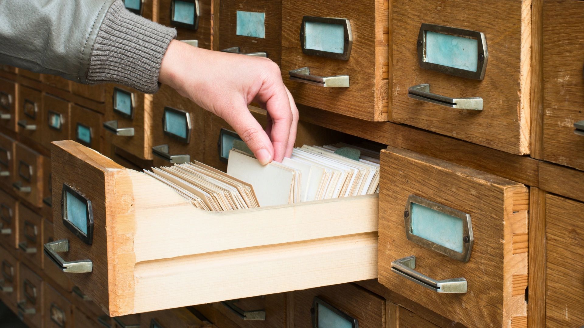 Researcher locating historical records in an archival card catalog and document filing system.