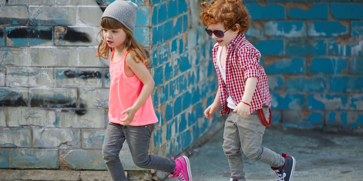 Two kids walking by a blue brick wall, one wearing a beanie and pink top.