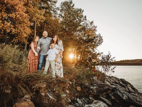 Family of four posing near a lakeside during autumn sunset.