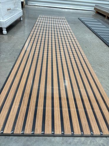 Long wooden slatted panel with black strips on concrete floor.