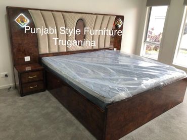 Punjabi style wooden bed with padded headboard and side drawers in a bright room.