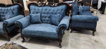 Elegant blue upholstered sofas with carved wooden frames in a showroom.