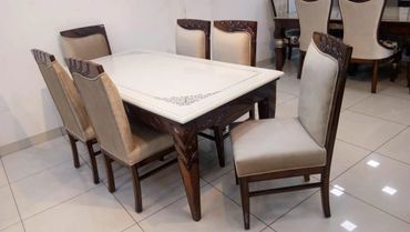 Elegant dining table set with beige cushioned chairs and intricate wooden detailing.
