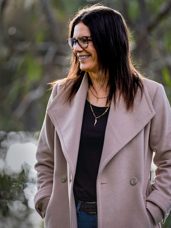 Smiling woman in glasses and beige coat outdoors.