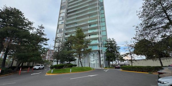 Modern high-rise building surrounded by trees and parked cars.