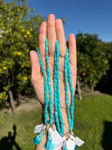 Hand holding four turquoise bead necklaces with tassels outdoors.