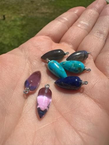 Hand holding various colorful gemstone pendants with metal loops.