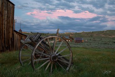 Old wooden wagon wheel on grassy field under cloudy sky.