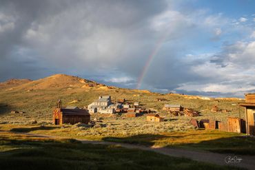 Old western town under a cloudy sky with a rainbow.