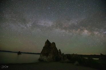 Starry night sky over rocky formations by the water.