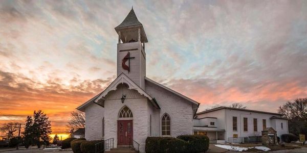 Historic white church with bell tower at sunset under a colorful sky.