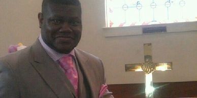 Man in a suit standing near a lit cross in a church.
